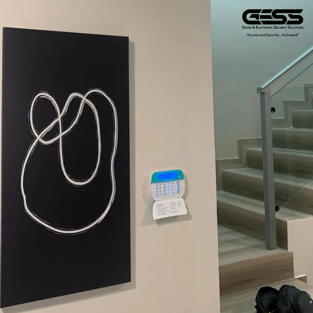 Backlit alarm keypad on a hallway wall beside a staircase