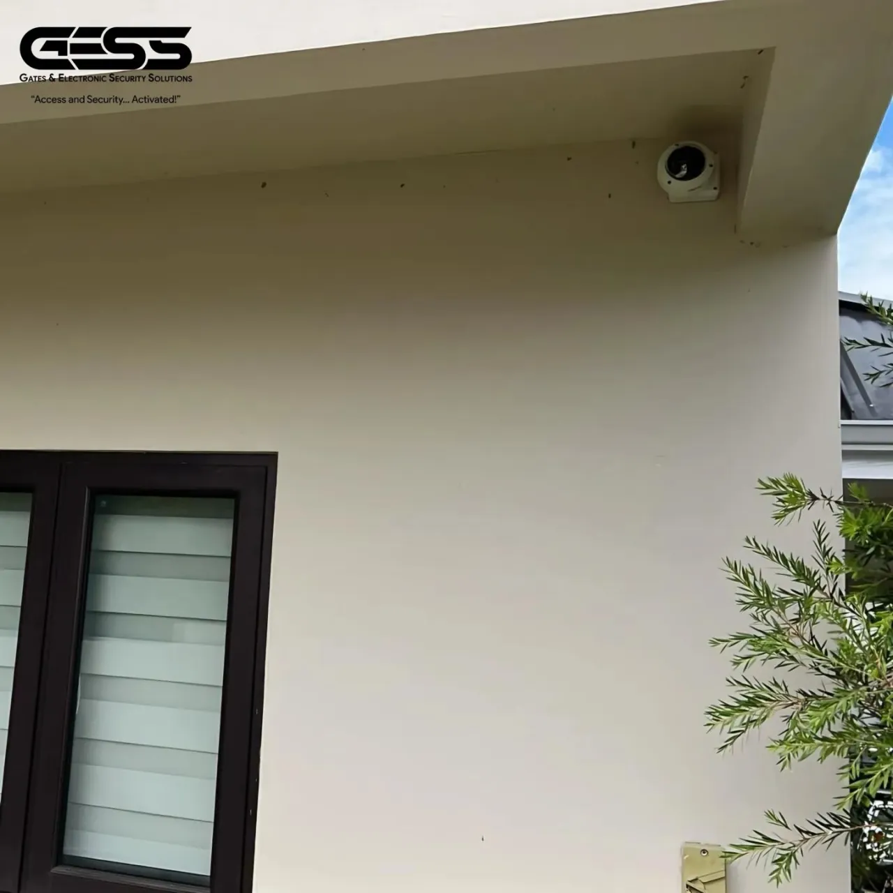 Small white camera tucked under the eave of a house beside a glazed door