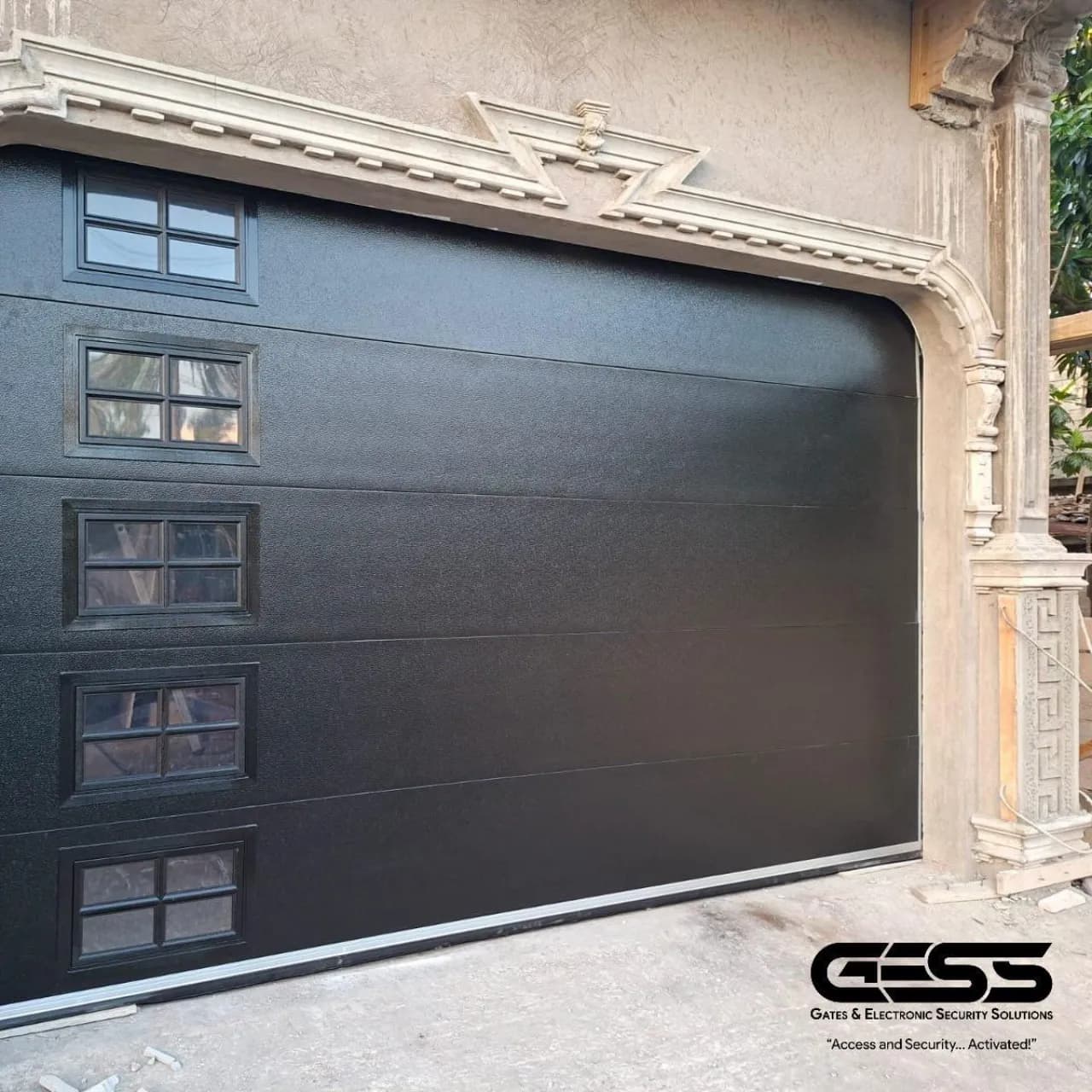 Black sectional garage door with windowed panels under a stone arch