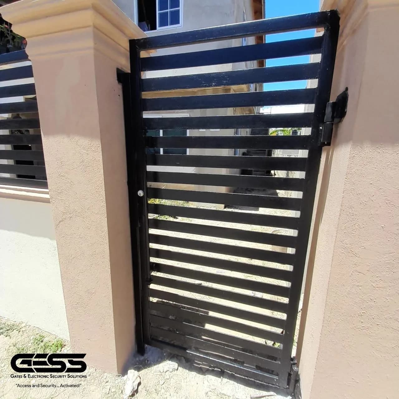 Black slatted pedestrian gate fitted between two rendered pillars