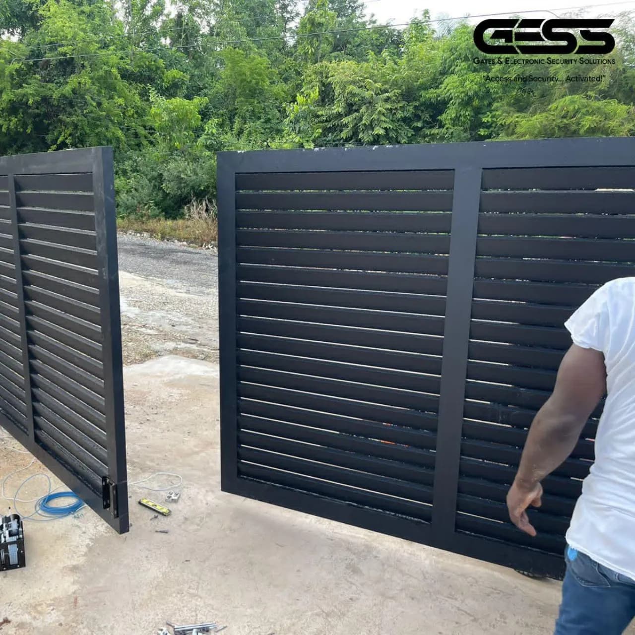 Two black slat gate panels standing on a driveway mid-installation