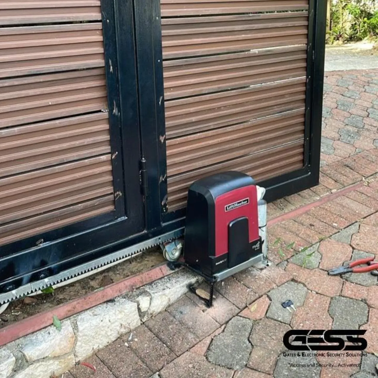 Red and black LiftMaster sliding gate motor mounted on a paved apron